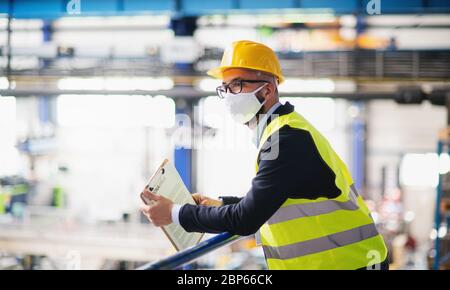 Tecnico o ingegnere con maschera protettiva e casco in piedi in fabbrica industriale. Foto Stock