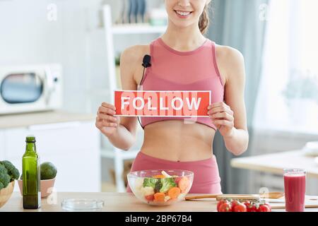 Ritratto di metà sezione della giovane donna in forma che tiene SEGUIRE segno e sorridendo alla macchina fotografica mentre cucinando cibo sano in cucina, copia spazio Foto Stock