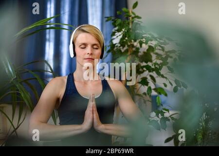 Vista frontale della giovane donna con le cuffie all'interno a casa, facendo esercizio di yoga. Foto Stock