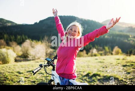 Donna anziana attiva con e-bike all'aperto in natura, braccia allungate. Foto Stock