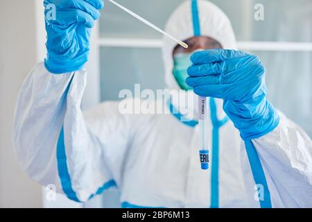 Medic in indumenti protettivi impacchi tampone per la gola dal campione di saliva per il test del coronavirus Foto Stock