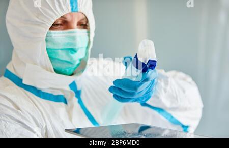 Un detergente in indumenti protettivi disinfetta il touchscreen dal tablet durante la pandemia di coronavirus Foto Stock