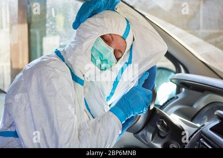 Stanco medico di emergenza dal servizio di ambulanza dorme sul volante in ambulanza mentre si sta in piedi vicino in indumenti protettivi Foto Stock