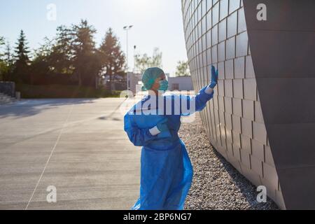 Il chirurgo in abbigliamento protettivo davanti alla clinica fa dei segnali manuali all'ingresso come un gesto durante la pandemia del coronavirus Foto Stock