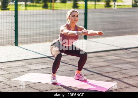 Intera lunghezza, donna con corpo atletico in stretto pantaloni allenamento  in tappetino esterno giorno d'estate, facendo squats con mani esteniche,  aerobica o pilates exe Foto stock - Alamy