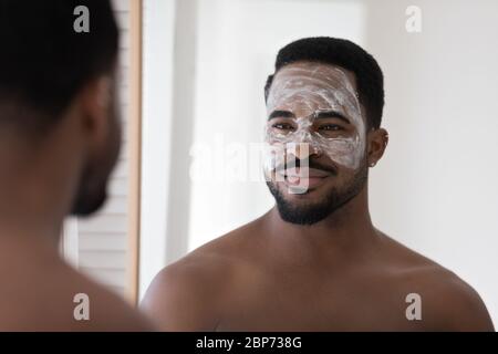 L'uomo afroamericano usa la maschera di bellezza facciale in bagno Foto Stock