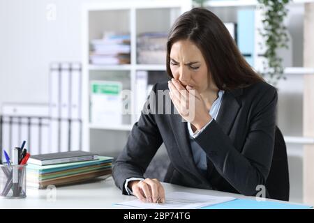 Donna dirigente stanca e in eccesso che brilica seduto su una scrivania in ufficio Foto Stock