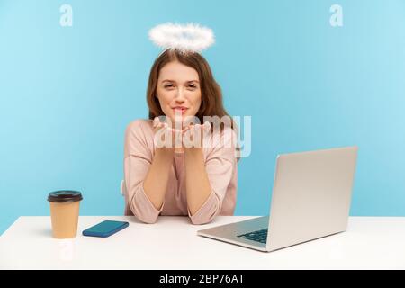 Bella donna angelica dipendente con nimbus seduto sul posto di lavoro e l'invio di bacio aria alla fotocamera, dimostrando sentimenti romantici, flirtare e sorridere. Foto Stock