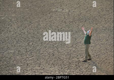 Uomo con maschera che prega da solo su suolo cracked Foto Stock