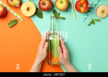 Le mani femminili tengono il flacone di sidro su sfondo a due toni. Composizione con sidro Foto Stock