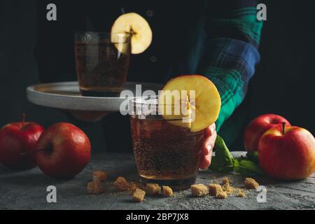 Femmina con vassoio per vetro di sidro. Composizione con sidro e mela su tavola grigia Foto Stock