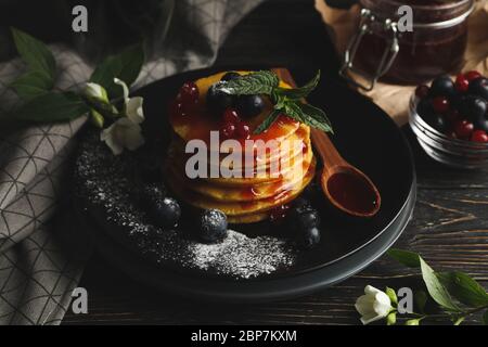 Piatto di gustosi pancake con frutti di bosco e polvere su tavolo di legno. Composizione di colazione dolce Foto Stock