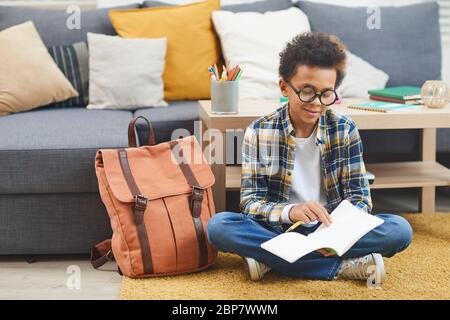 Ritratto a lunghezza intera di cute afroamericano ragazzo scrittura in notebook mentre seduto sul pavimento a casa, spazio di copia Foto Stock