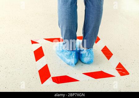 Donna stare in linea mantenendo la distanza sociale indossare copriscarpe, copriscarpe mediche in negozio, supermercato, ospedale. Persone che si trovano dietro un avvertimento Foto Stock