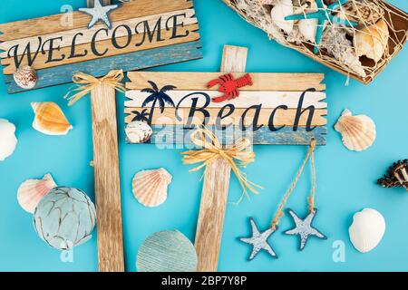 Cartelli in legno danno il benvenuto alla spiaggia e alle conchiglie su sfondo blu. Foto Stock