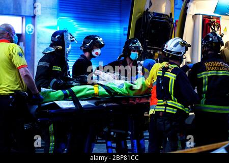 Una persona anziana sospettata di avere Corvid-19 è aiutata in un'ambulanza da vigili del fuoco e operatori sanitari. Foto Stock