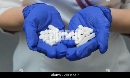 Giovane donna medico in camice medico bianco e guanti blu gomma tiene un sacco di compresse bianche pillole nel palmo delle sue mani. Concetto di salute, droga, Foto Stock