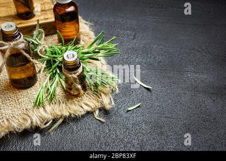 Rami di erbe di rosmarino e bottiglie di olio essenziale di rosmarino su fondo di pietra nera. Concetto di aromaterapia erboristica. Foto Stock