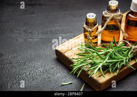 Rami di erbe di rosmarino e bottiglie di olio essenziale di rosmarino su fondo di pietra nera. Concetto di aromaterapia erboristica. Foto Stock