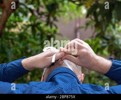 Vista posteriore di un uomo calvo che mette su una maschera di faccia e legandolo in su dietro la sua testa Foto Stock