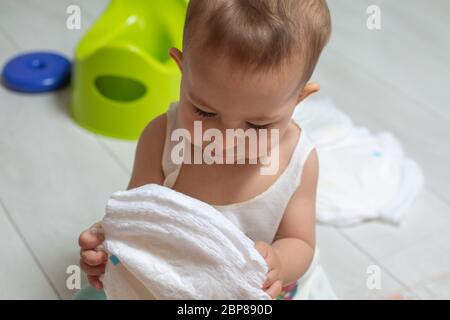 Il concetto di imparare ad usare il vaso da camera. Primo piano: Un bambino carino tiene i pannolini puliti nelle mani e li guarda. Sullo sfondo a Foto Stock