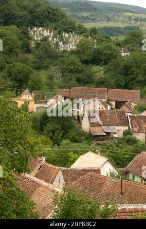 Vista su un antico villaggio tradizionale sassone nella regione di Sibiu, Transilvania, Romania, e un cimitero sulla collina Foto Stock