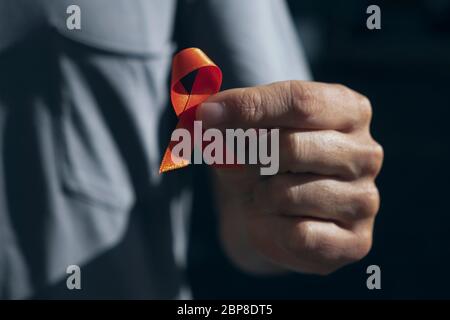 primo piano di un giovane caucasico con un nastro arancione in mano, a sostegno delle persone affette da sclerosi multipla Foto Stock