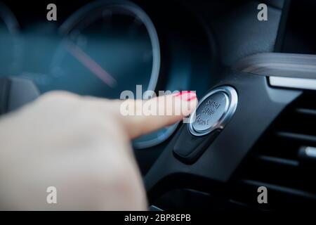 il dito femminile preme il pulsante start stop engine sul cruscotto di un'auto. primo piano, messa a fuoco morbida, sullo sfondo il cruscotto e il tachimetro dell'auto sono sfocati Foto Stock