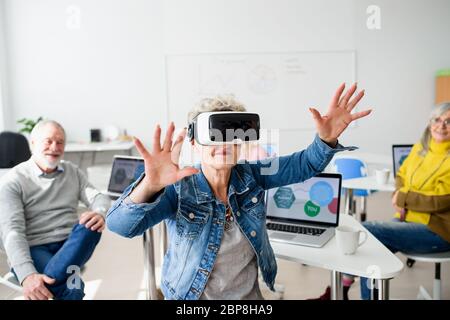 Gruppo di anziani con occhiali di protezione VR in classe informatica e tecnologica. Foto Stock