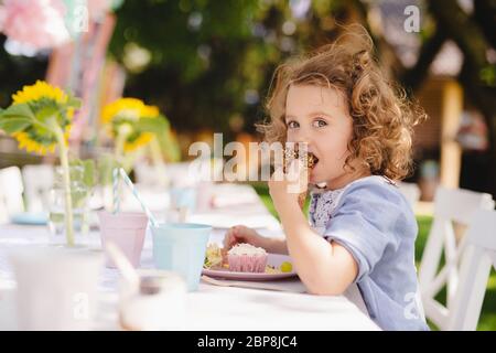 Piccola ragazza seduta all'aperto in giardino in estate, mangiare spuntini. Foto Stock