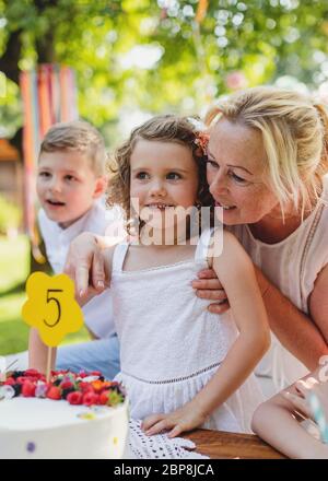 Piccola ragazza con torta che festeggia il compleanno all'aperto in giardino in estate, concetto di festa. Foto Stock
