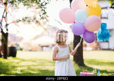 Piccola ragazza all'aperto in giardino in estate, giocando con palloncini. Foto Stock