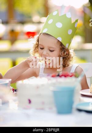 Piccola ragazza seduta all'aperto in giardino in estate, mangiare torta. Foto Stock