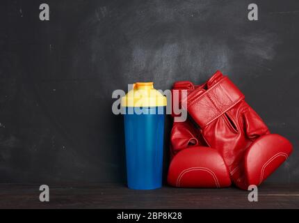 coppia di guanti da boxe in pelle rossa e bottiglia in plastica blu su sfondo nero, attrezzature sportive, spazio per fotocopie Foto Stock