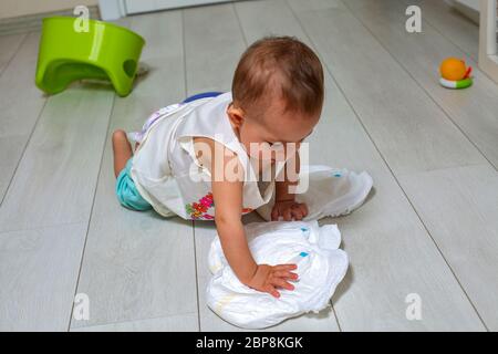 un piccolo bambino carino gioca con nuovi pannolini puliti sul pavimento di rhe whit. sullo sfondo un piatto da camera e giocattoli in sfocatura. Il concetto di apprendimento da utilizzare Foto Stock