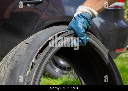 ruota rotta. la mano del maestro in un guanto blu tiene la ruota strappata con il filo. primo piano. sullo sfondo auto nera in sfocatura Foto Stock