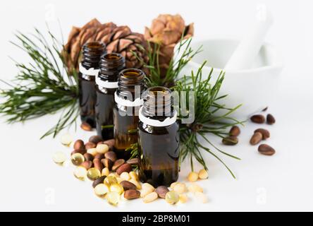 concetto di prodotto naturale, composizione di bottiglie di vetro con olio, cedro, capsule noci e malta su fondo bianco Foto Stock