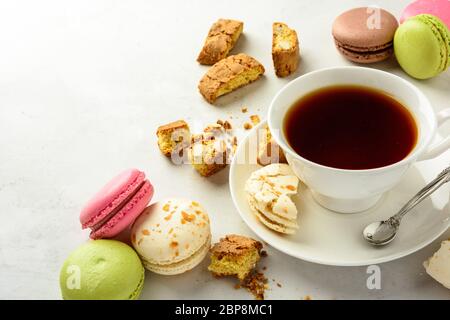 Tazza di tè nero con gustosi biscotti alle mandorle, ricchi di vitamine, minerali e macaroоns varicolored su fondo bianco in chiave chiara. Spazio di copia. Foto Stock