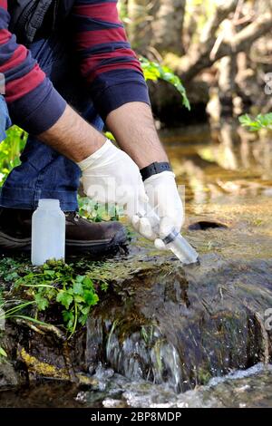 Il biologo che raccoglie campioni in un corso d'acqua per l'analisi del suo inquinamento e per lo studio delle sue caratteristiche. Foto Stock