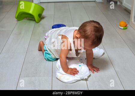 concetto di addestramento del vasino. Un bambino carino in una stanza sul pavimento luminoso gioca con un pannolino e un pentola verde invertito. Messa a fuoco morbida Foto Stock