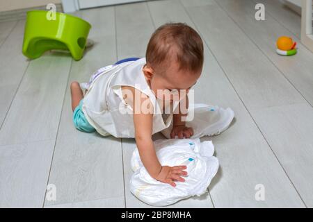 concetto di addestramento del vasino. Un bambino carino in una stanza sul pavimento luminoso gioca con un pannolino e un pentola verde invertito. Messa a fuoco morbida Foto Stock