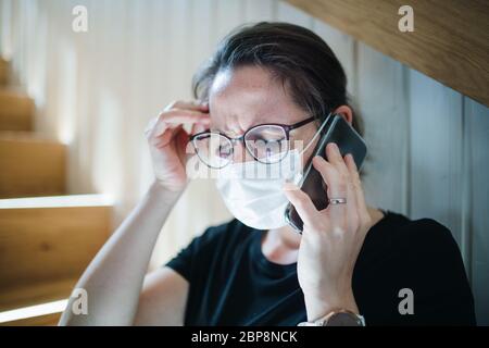 Donna preoccupata con telefono e maschere al chiuso a casa, concetto di virus Corona. Foto Stock