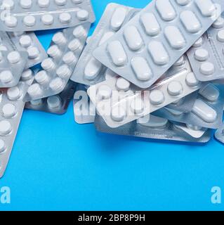Diverse compresse di colore bianco in un pacchetto sono sparse su uno sfondo blu Foto Stock