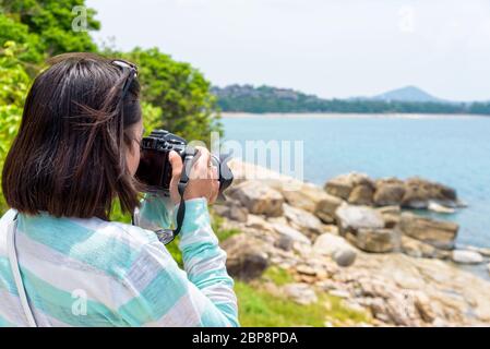 Giovane donna era felice per la fotografia con la fotocamera DSLR sulla roccia vicino al mare sotto il cielo di estate a Koh Samui Island, Surat Thani provincia, Tailandia Foto Stock