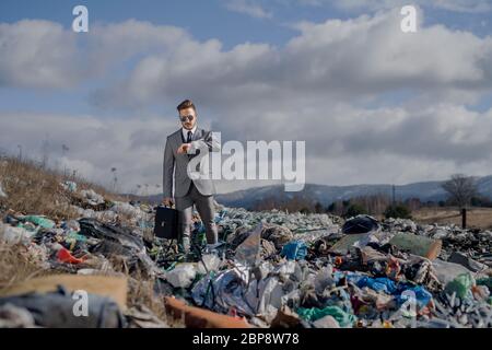 Uomo d'affari moderno in discarica, consumismo contro concetto di inquinamento. Foto Stock