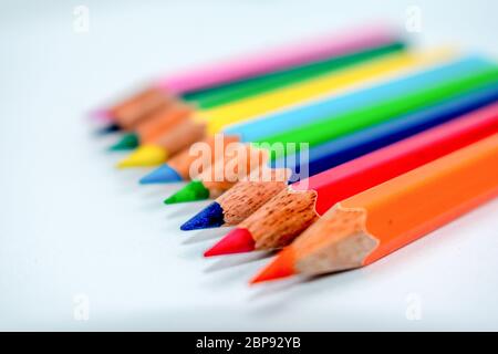 In piedi fuori dalla folla del concetto. Mazzetto assortiti di multi matite colorate matite colorate a disposizione arcobaleno su sfondo bianco, piatto laici. Geometria pa Foto Stock