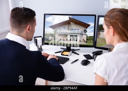 Vista posteriore del maschio e femmina agente immobiliare cerca casa modello sullo schermo del computer Foto Stock