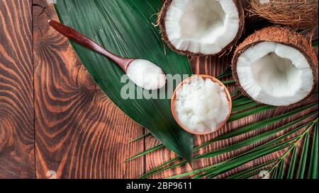 Vista dall'alto dell'olio MCT di cocco nel recipiente e nel cucchiaio e noce di cocco dimezzata sul tavolo di legno. Benefici per la salute dell'olio MCT. Trigliceridi a catena media o MCT, f Foto Stock