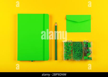Ben organizzato di cancelleria laici piana di notebook ecocompatibile, Busta, matita, ufficio clip, leganti e i pin nella casella su giallo Foto Stock