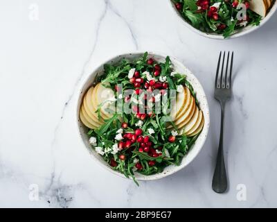 Vegan insalatiera con foglie di rucola, pera, melograno, cocco sbriciolate o ricotta sul tavolo di marmo. Colazione Vegana Vegetariana Cibo, dieta concetto Foto Stock